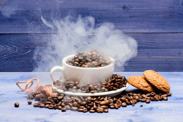 Cafe drinks menu. Fresh roasted coffee beans. Coffee for inspiration and energy charge. Degree of roasting grain. Cup full coffee brown roasted beans white clouds of smoke blue wooden background
