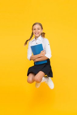 Okul konseptine geri dönelim. Küçük kız sarı arka plan. Okul kızı okumayı seviyor. Duygusal öğrenci. Eğitim için heyecanlıyım. Okul üniforması giyen mutlu çocuk. Eğleniyor. Atlama ve özgür hissetmek