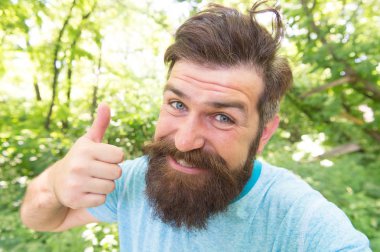 Yüz şekli için mükemmel saç uzunluğu. Tarz saçlı mutlu adam el gibi veriyor. Yaz doğası üzerine şık bıyık ve sakal saçlı tüylü adam. Sakallı hipster gülümsemeci yüz saçları ile gülümsüyor