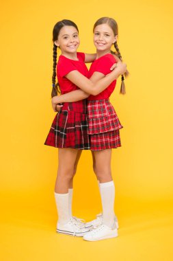 Birlikte mutlu. Okul kızları birlikte eğleniyor. Sevimli küçük kızlar sarı arka plan gülümsüyor. Aynı kıyafetler giyen mutlu küçük kızlar. Arkadaşlar dostluk zevk. Gerçek arkadaşlar. Neşeli arkadaşlar