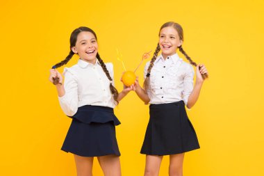 Okul diyeti. İlköğretim öğrencileri sarı arka planda portakal meyvelerinden meyve suyu içiyor. Sağlıklı okul atıştırmalıkları eşliğinde küçük çocuklar. Vitamin zengin içki giyen okul üniformalı küçük kızlar