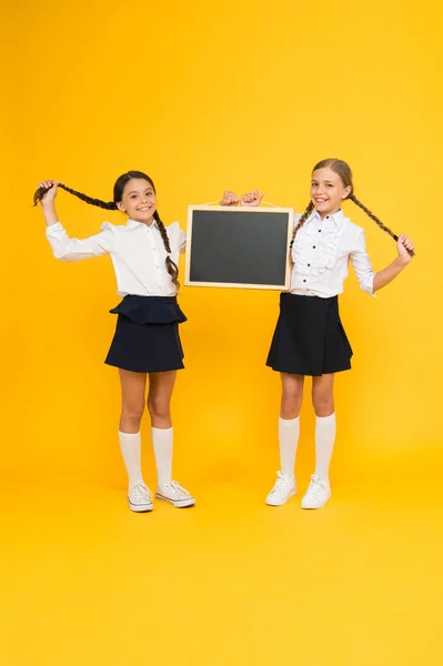 Cabelo mais saudável da raiz à ponta. Bonito crianças pequenas com cabelos entrançados segurando quadro preto no fundo amarelo. Meninas felizes com tranças de cabelo comprido e quadro-negro. Cabelo trançado para a escola — Fotografia de Stock