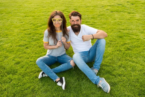 Tornando o dia dos namorados divertido. Casal apaixonado segurando adereços de festa de namorados extravagantes em paus. Hipster e menina sexy olhando através de óculos extravagantes para dia dos namorados. Celebrar o dia dos namorados juntos — Fotografia de Stock