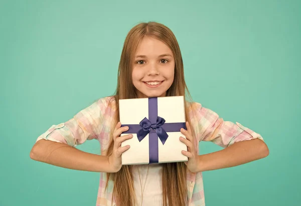 Приятный подарок. Маленький шопоголик с подарком, завернутым в коробку. Маленький ребенок держит подарочную коробку, привязанную ленточкой. Милый покупатель наслаждается покупками. Маленькая девочка после покупки подарка — стоковое фото