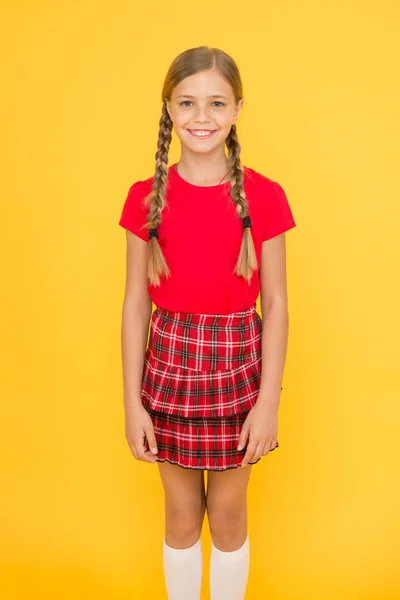 Αξιολάτρευτο γλυκούλι. Χαριτωμένο κοριτσάκι γοητευτικό χαμόγελο σε κίτρινο φόντο. Ευτυχισμένο μικρό κορίτσι φορώντας κόκκινα ρούχα. Κορίτσι με πλεκτά μαλλιά μακριά πλεξούδες. Αξιολάτρευτο κορίτσι περήφανη να είναι μαθήτρια. Ευτυχισμένη παιδική ηλικία — Φωτογραφία Αρχείου