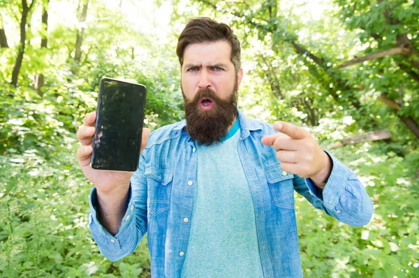 no connection. angry bearded manon phone. Mature hipster with beard pointing finger. got lost in forest. brutal man with phone. hipster style. guy in forest use gps navigation. summer camping