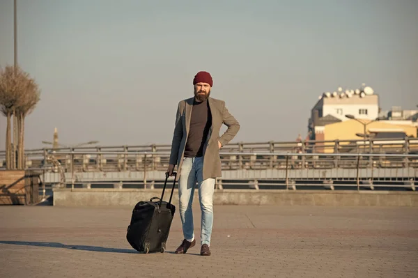 Moving to new city alone. Hipster ready enjoy travel. Carry travel bag. Man bearded hipster travel with luggage bag on wheels. Traveler with suitcase arrive airport railway station urban background