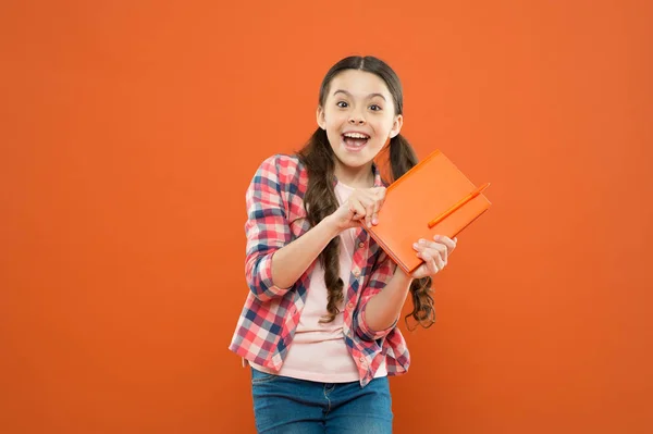 Librería. colegiala leer libro sobre fondo naranja. lección de literatura. de vuelta a la escuela. niña feliz con cuaderno. escribiendo notas. Diario de niños. poesía y novela. educación moderna — Foto de Stock