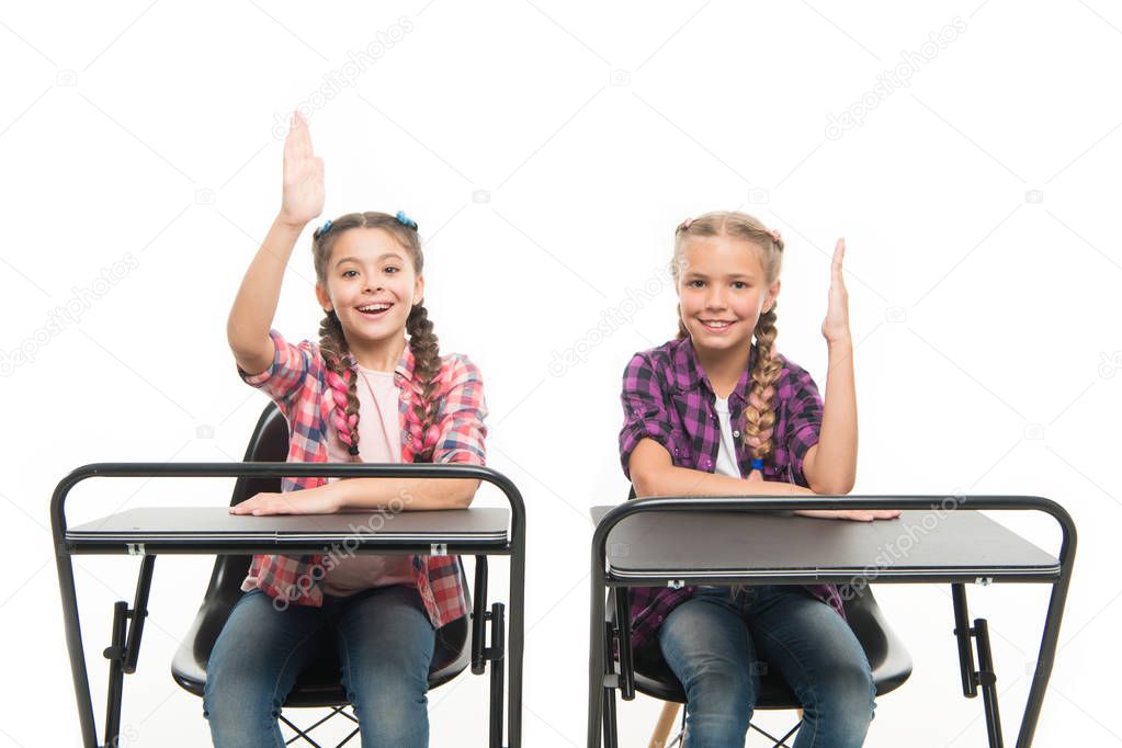 Free or private schooling. Little children enjoy home schooling. Small schoolgirls having compulsory schooling. Adorable kids with raised hands sitting at desks isolated on white. Schooling years
