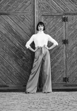 Moda ve stil konsepti. Makyajlı kız moda kıyafetlerle poz yapıyor. Moda kıyafeti ince uzun boylu bayan. Kadın kendinden emin bir şekilde yürüyor. Kadın şık esmer standı açık ahşap arka plan