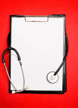 Kırmızı arka plan kopyalama alanı üzerinde fonndoskop ve kağıt tablet. Hastalığın geçmişi. Tıbbi tedavi. Tıp kavramı. Tıbbi yardım ve konsültasyon. Poliklinik ve hastane. Sağlık sigortası