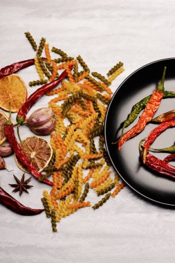 Kırmızı biber ve siyah seramik tabak içinde makarna ve malzemeler.