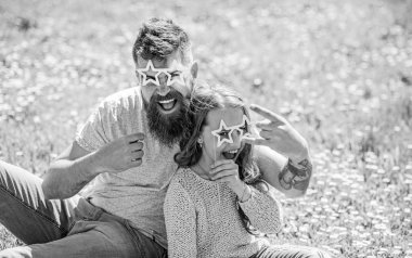 Rock yıldız kavramı. Çocuk ve yıldız şekilli eyeglases photo booth özniteliğine çayır ile poz baba. Baba ve kızı, grassplot, arka planı yeşil çimenlerin üzerinde oturur. Aile harcamak açık havada eğlence