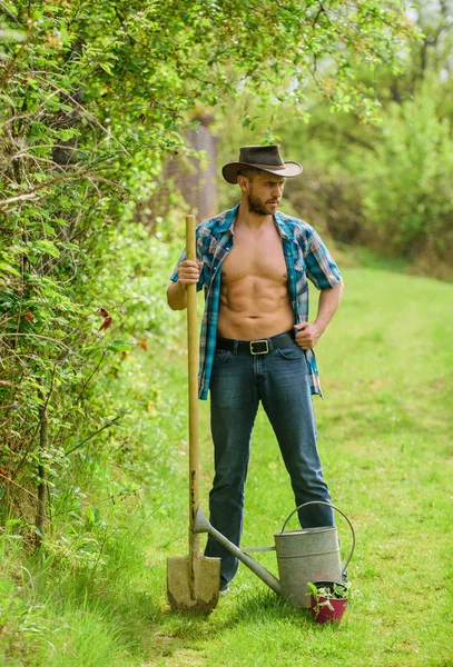 sexy farmer hold shovel and watering can. muscular ranch man in cowboy hat. happy earth day. Eco living. farming and agriculture cultivation. Garden equipment. Eco farm. Harvest. Warn atmosphere