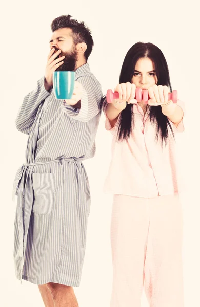 Couple, family offers alternative energy source. Couple in love in pajama, bathrobe stand isolated on white background. Girl with dumbbell, man with coffee cup. Alternative lifestyle concept