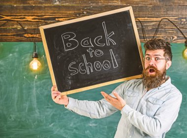 Gözlük öğretmen okul için başlıklı yazı tahtası tutar. Adam sakal ve bıyık sürpriz yüz memnuniyetle öğrencilerin, kara tahta arka plan ile. Lise kavramı