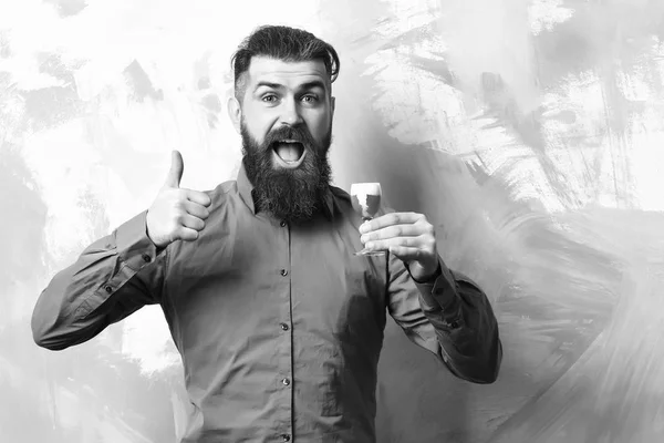 Bearded man, long beard. Brutal caucasian smiling happy hipster with moustache in brown shirt holding alcoholic red shot on colorful texture backgroun