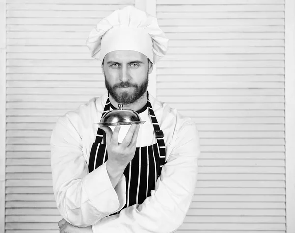 男のコック帽子とエプロンは、ふたで覆われて食事を保持します。おいしい食事のプレゼンテーション。高級料理には、細心の準備と慎重なプレゼンテーション食事が特徴。秘密の食事プレゼンテーション。シェフの料理 — ストック写真