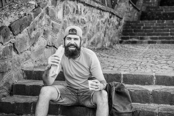 Läcker mat som passar hans livsstil. Kaukasisk kille resenär njuter av gatumat köket. Skäggiga man äter ohälsosam skräpmat. Hipster vilar och har varmkorv snabbmat under sommaren reser — Stockfoto