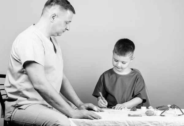 Boy cute child and his father doctor. Hospital worker. First aid. Medical help. Trauma and injurie. Medicine concept. Kid little doctor sit table medical tools. Health care. Medical examination