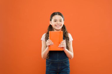 Çocuk edebiyatı. dizüstü bilgisayar ile mutlu küçük kız. edebiyat dersi. okul kız turuncu arka plan kitap okuyun. şiir ve roman. modern eğitim. notlar yazma. çocuk günlüğü. okula geri dön