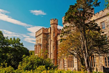 Victoria tarzı mimari ve tasarım. Stornoway, Birleşik Krallık, bahçede Lews Castle. Castle ile mavi gökyüzü üzerinde yeşil ağaçlar. Simgesel Yapı ve cazibe. Yaz tatil ve yolculuk tutkusu
