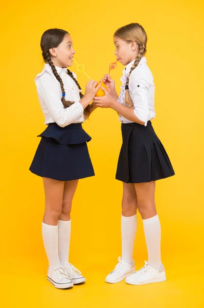 Το πορτοκαλί είναι το πιο υγιές υγρό. Μικρά κορίτσια πίνουν χυμό από πορτοκαλί φρούτα σε κίτρινο φόντο. Μικροί μαθητές απολαμβάνουν ζουμερό πορτοκαλί σνακ. Χυμός πορτοκαλιού γεμάτος βιταμίνη — Φωτογραφία Αρχείου