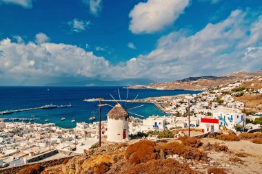 Mykonos, Yunanistan üzerinden deniz manzarası. Köy fırıldak dağ manzara mavi deniz üzerinde. Güzel mimari ile bulutlu gökyüzü üzerinde beyaz ev sahipliği yapmaktadır. Yolculuk tutkusu ve seyahat. Bir Akdeniz Adası yaz tatili