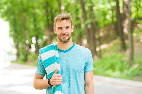 Healthy and active. Blond man. Handsome man wearing casual tshirt with towel on natural landscape. Man with unshaved face hair and stylish haircut. Caucasian man on summer day