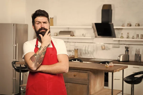 Чоловік бородатий гіпсовий червоний фартух стоїть на кухні. Кухонний магазин меблів. Готуємо на новій кухні. Потрібне кулінарне натхнення. Вихідні починаються зі смачного сніданку. Як перетворити кулінарію в звичку — стокове фото