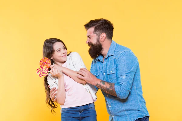 Dulce postre. Un buen padre hipster barbudo para una hija adorable. Dulce infancia. Niña y papá sostienen piruletas de colores. Compartiendo dulces con la gente más querida. Hija y padre comen dulces dulces — Foto de Stock