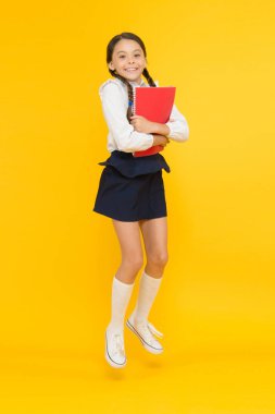 Duygusal öğrenci. Eğitim için heyecanlıyım. Okul üniforması giyen mutlu çocuk. Eğleniyor. Zıplamak ve özgür hissetmek. Okul konseptine geri dönelim. Küçük kız sarı arka plan. Okul kızı okumayı seviyor
