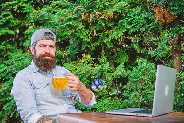 Ele merece esta cerveja. Brutal homem lazer com cerveja e jogo online. Finalmente sexta-feira. Hipster relaxar sentar terraço ao ar livre com cerveja. Freelancer hipster barbudo desfrutar de fim de dia de trabalho com caneca de cerveja — Fotografia de Stock