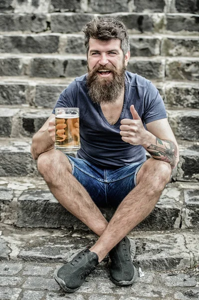 Hipster relaxed drinking beer outdoor. Light ales or dark stouts drink them all. Man with beard and mustache hold beer glass outdoors. Cafe summer terrace. Guy having rest with cold draught beer