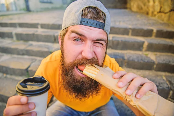 A comer depressa. Homem barbudo a comer sanduíche de cachorro quente. O caucasiano gosta de comer fora. Hipster comer cachorro quente e descansando em escadas ao ar livre — Fotografia de Stock