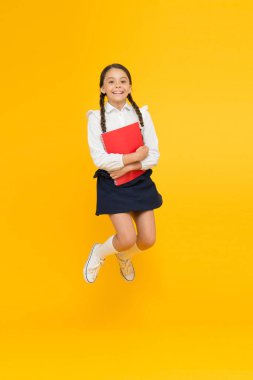 Eğitim için heyecanlıyım. Okul üniforması giyen mutlu çocuk. Eğleniyor. Zıplamak ve özgür hissetmek. Okul konseptine geri dönelim. Küçük kız sarı arka plan. Okul kızı okumayı seviyor. Duygusal öğrenci