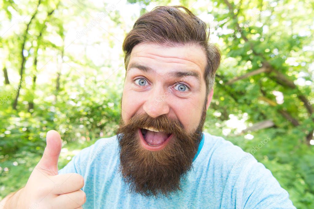 Thumbs up for bearded and beardy. Bearded man giving thumbs up hand gesture on natural landscape. Bearded hipster gesturing on summer day. Brutal guy wearing mustache and beard on bearded face