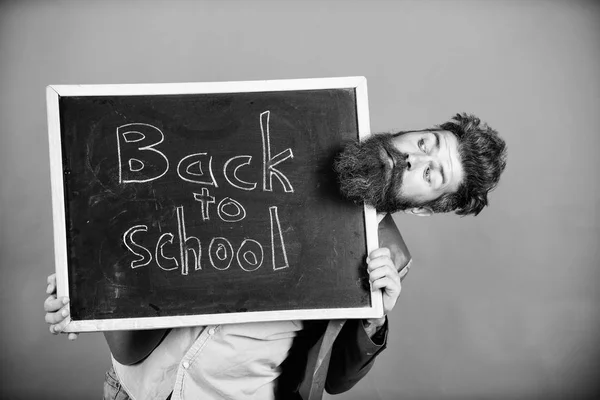 Schule und Lehrer warten auf Sie. Lehrer oder bärtige Pädagogen stehen auf und halten eine Tafel mit der Aufschrift zurück zum schulroten Hintergrund. Lehrer informiert zurück zum Studium, Schuljahr beginnt — Stockfoto