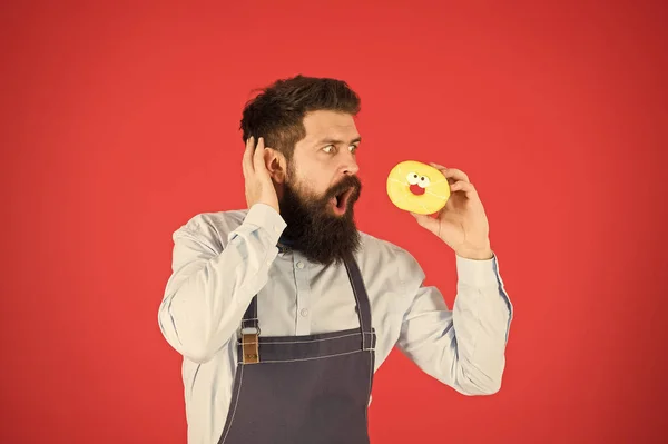 Pas du tout. De vrais faits sur le sucre. Hipster barbu boulanger tenir beignet glacé sur fond rouge. Café et concept de boulangerie. Doux beignet du boulanger. Homme barbu boulanger dans tablier de cuisine tenir dessert mignon — Photo