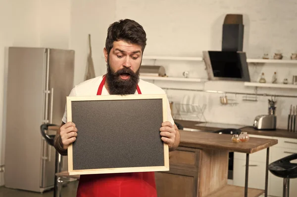 Secret tips. Useful information. Man bearded hipster red apron stand in kitchen. Kitchen furniture store. Kitchen hacks concept. Clever ways to organize kitchen. Cook hold blank chalkboard copy space