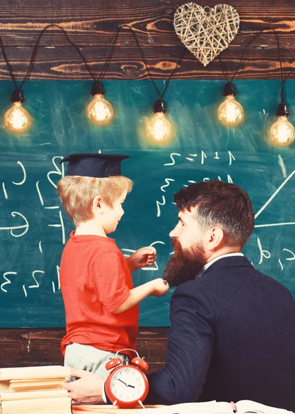 神童儿童概念。老师带着胡子, 父亲在教室里教小儿子, 黑板上的背景。男孩, 孩子在研究生盖帽讨论黑板上的涂鸦, 而教师听 — 图库照片