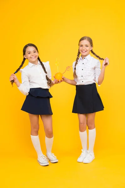 Iedereen houdt van een frisse kapsel. Kleine meisjes met lange kapsel drinken natuurlijk sap op gele achtergrond. Kleine kinderen met gevlochten kapsel genieten van Oranje drankje. Kapsel geschikt voor school — Stockfoto