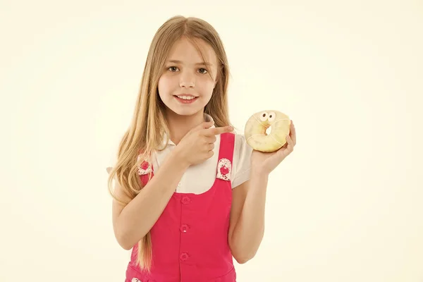 Meisje met grote glimlach holding donut. Geanimeerde dessert, geglazuurde bagel met ogen. Kid wijzend op zoete behandelen, zoete tand hemel. Kind met lang haar dragen van roze outfit geïsoleerd op witte achtergrond — Stockfoto