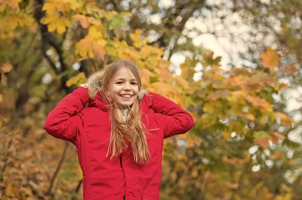 暖かいジャケットに居心地の良い感じ。フード付け女の子幸せ摩耗コートでは、秋の自然をお楽しみください。子供は、秋のシーズンのコートを着用します。秋の服とファッションのコンセプト。歩く子金髪長い髪秋公園背景 — ストック写真