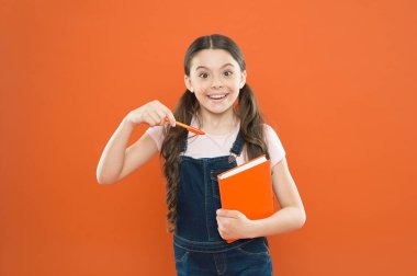 Çok ilginç bir kitap. edebiyat dersi. Okula geri dön. dizüstü bilgisayar ile mutlu küçük kız. şiir ve roman. modern eğitim. notlar yazma. çocuk günlüğü. okul kız turuncu arka plan kitap okumak