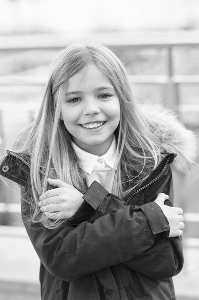 子供の笑顔の女の子はフードに毛皮のコート ジャケットを着用が冷たく感じる。寒い天候の概念。彼女は凍結します。赤ちゃんは寒さのため自分を抱擁します。子供は、屋外のウォーム アップしようとします。冬の寒い季節に落ちる — ストック写真