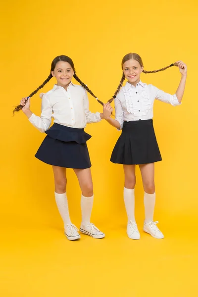 Coiffure parfaite pour les écolières parfaites. Adorables petites filles avec une coiffure longue sur fond jaune. Petits enfants mignons tenant coiffure tressée. Obtenir votre coiffure pour durer toute la journée — Photo