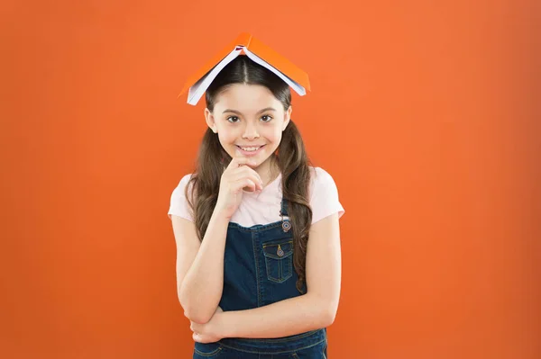 Homeschooling en privéles. Boek op haar hoofd. Kleine meisje boek dak hoofd. Kleine meisje boek oranje achtergrond. Interessant verhaal voor Kid. Studeren en ontspannen. Studeren thuis. Huiswerk concept — Stockfoto