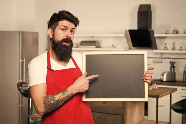 Kitchen furniture store. Kitchen hacks concept. Clever ways to organize kitchen. Cook hold blank chalkboard copy space. Secret tips. Useful information. Man bearded hipster red apron stand in kitchen