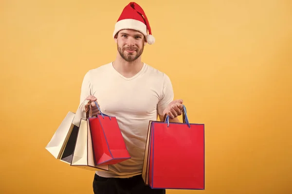 Mann mit Weihnachtsmütze hält Weihnachtsgeschenk in der Hand. Weihnachtseinkauf im Internet. Frohes neues Jahr. Lieferung Weihnachtsgeschenke. glücklicher Weihnachtsmann auf gelbem Hintergrund. am Morgen vor Weihnachten. Frohe Weihnachten — Stockfoto